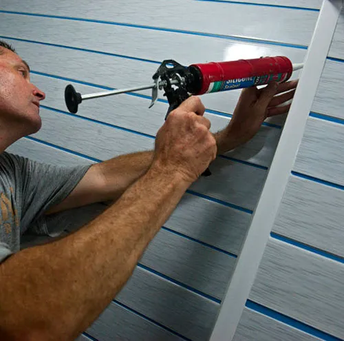 A professional house painter applying caulk to trim on a home's exterior