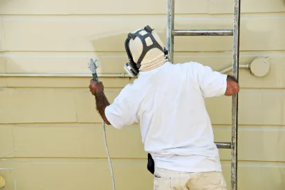 Professional painter using a paint gun to paint exterior of a home.