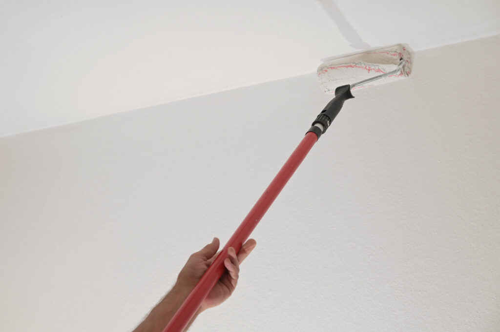 A person paints a ceiling white using a brush roller