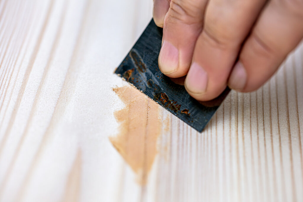 A person is using a scraper to apply wood filler