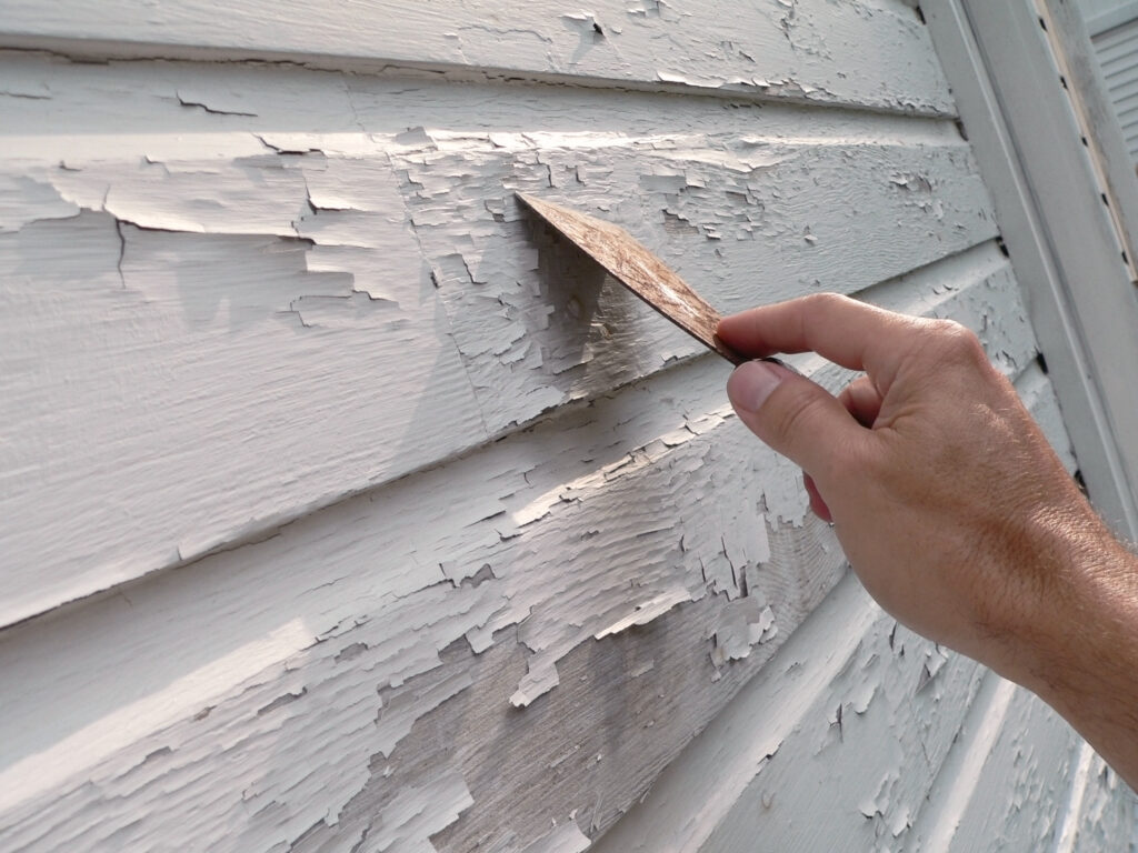 A person uses a scraper to take off old, peeling paint